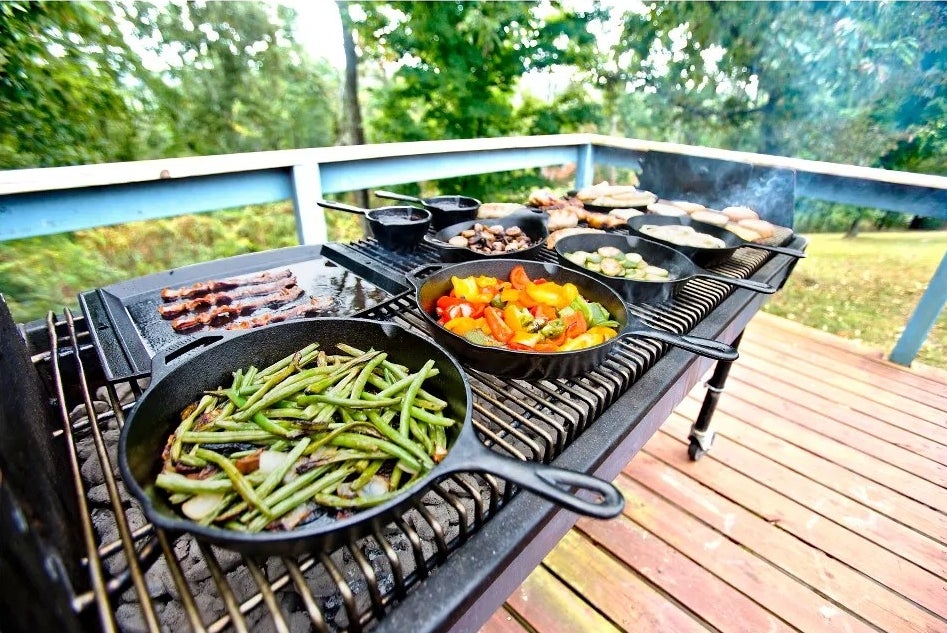 The skillet on a charcoal grill outside, cooking green beans