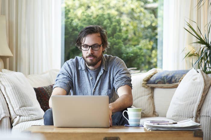 A man types on his laptop while sitting on the couch