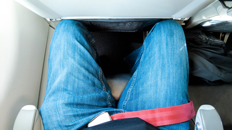 A man&#x27;s knees pressed against the seat in front of him on a plane