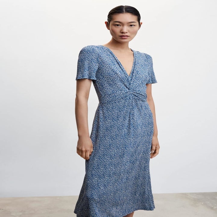 A model in a blue printed short sleeve dress with twist front detail and v neck