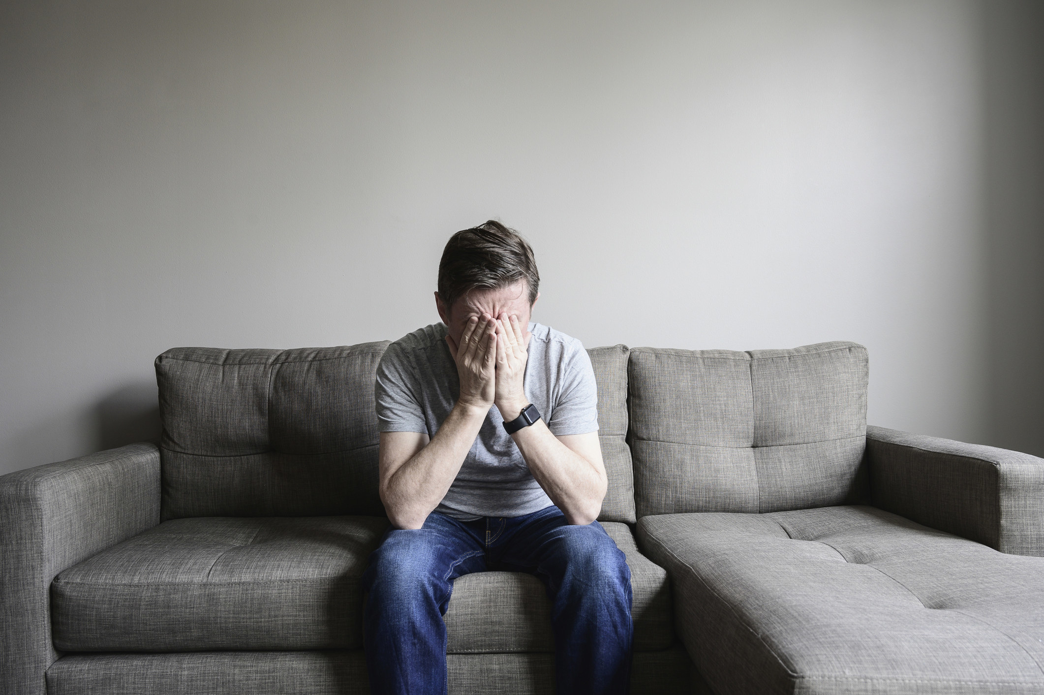 person with their face in their hands as they sit on the couch