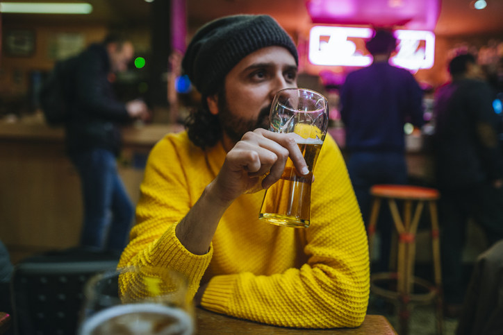 A man alone at a bar drinking a beer