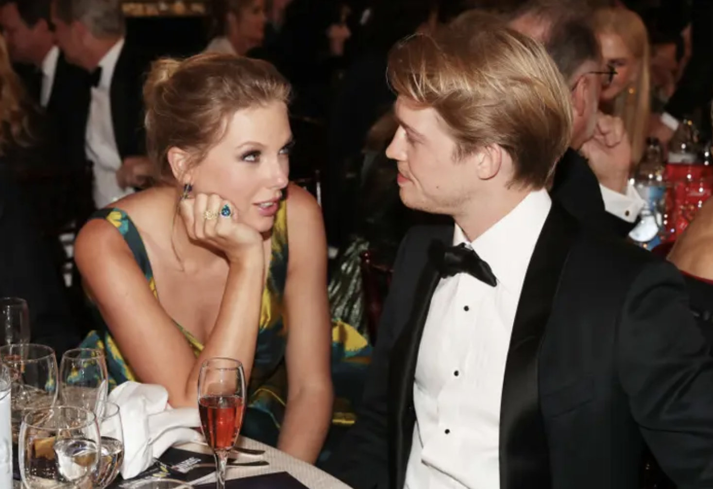 Taylor Swift smiles at Joe Alwyn sitting at a table at a formal event
