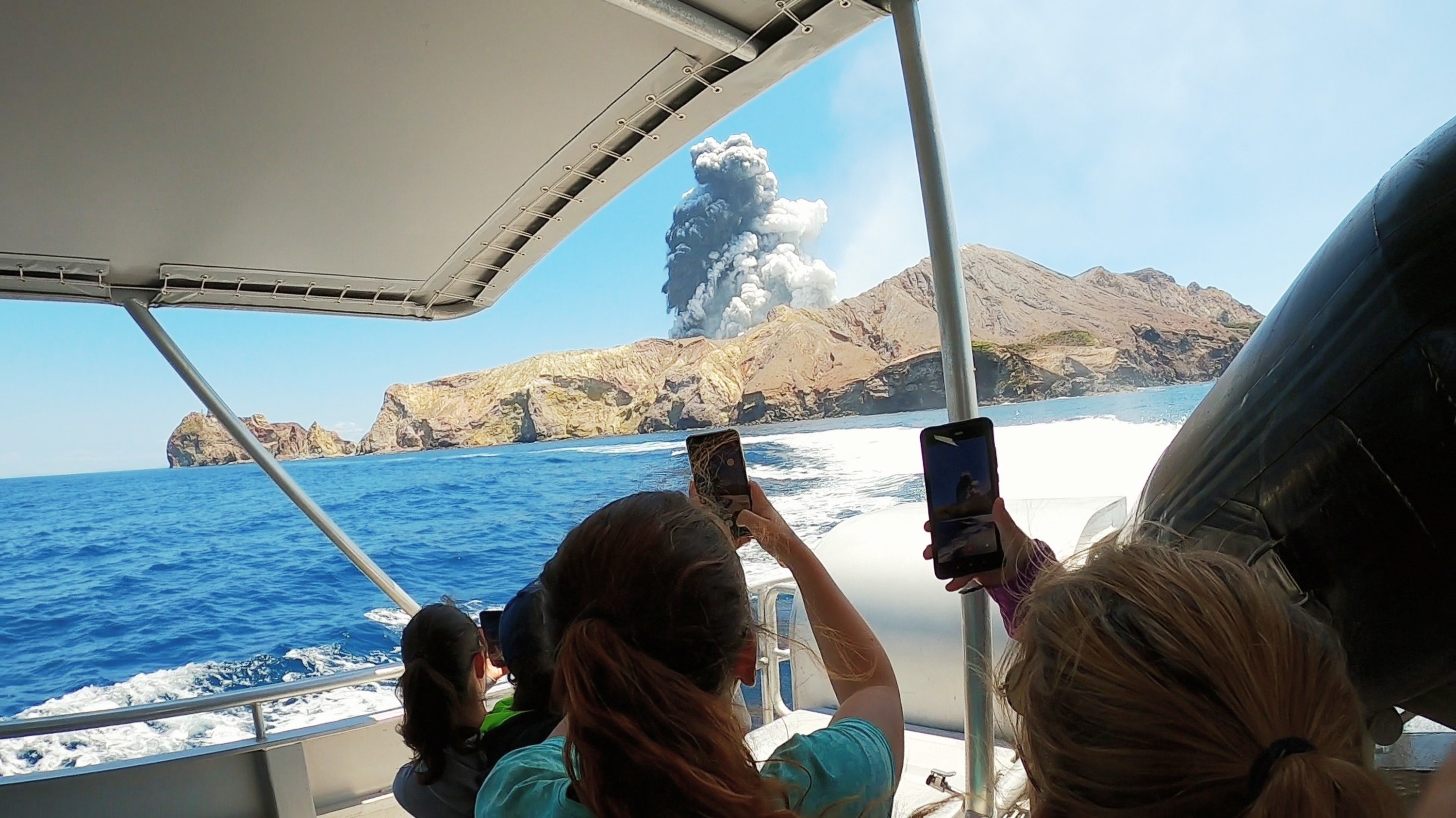 People on a boat use their phones to photograph Whakaari volcano on White Island in New Zealand