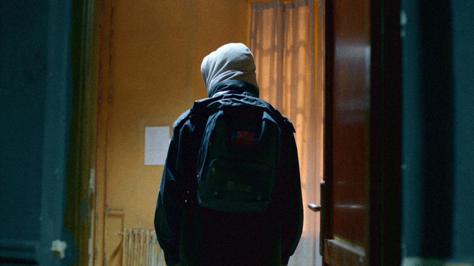 A man in a hood with a backpack walks away from the camera
