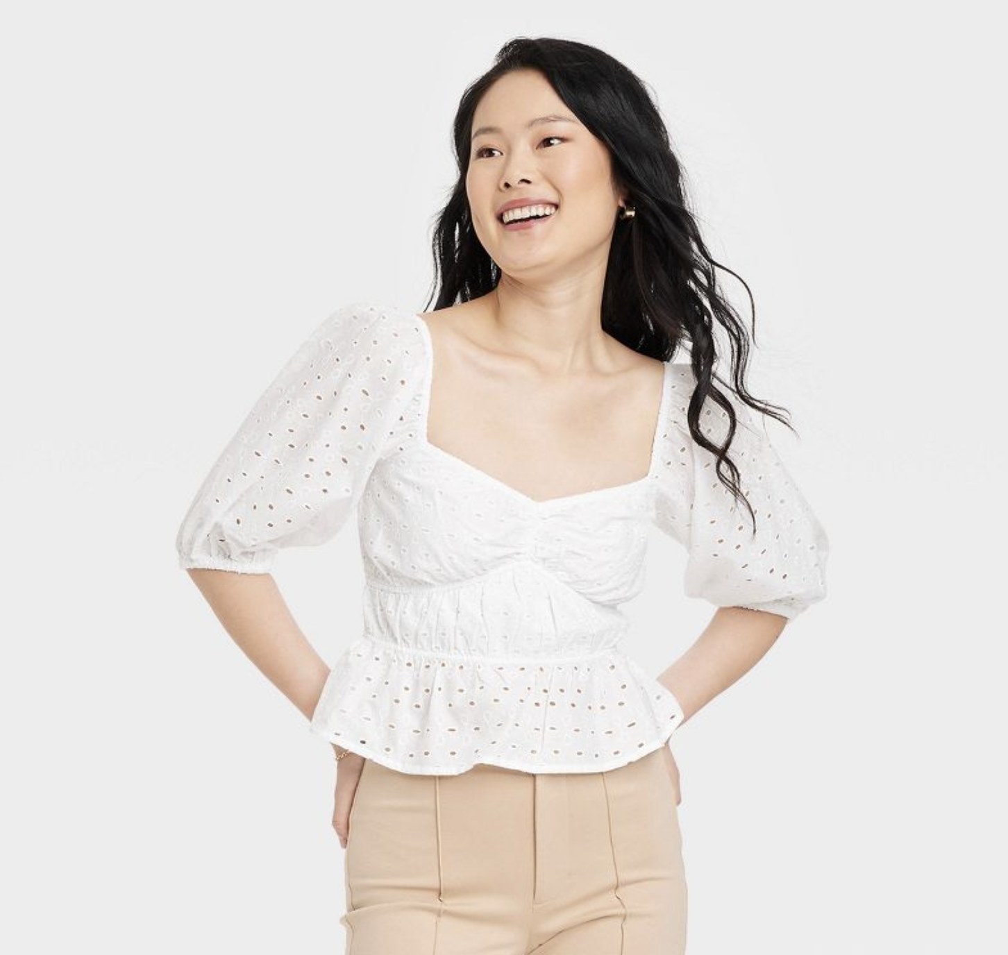 A person with long black hair wearing a white peplum blouse