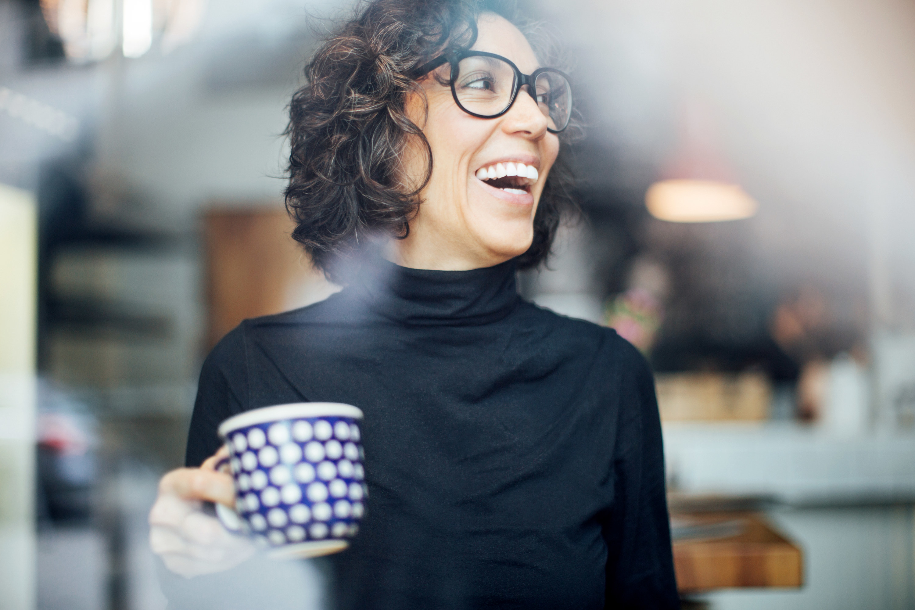 woman laughs while holding a glass mug