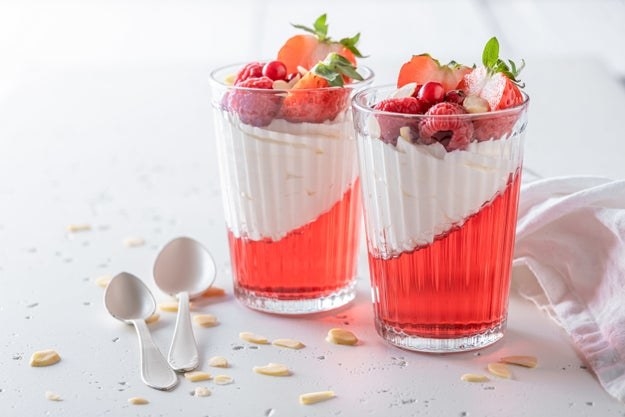 Two glass cups filled with jello, cream and strawberries sit between a napkin and two spoons