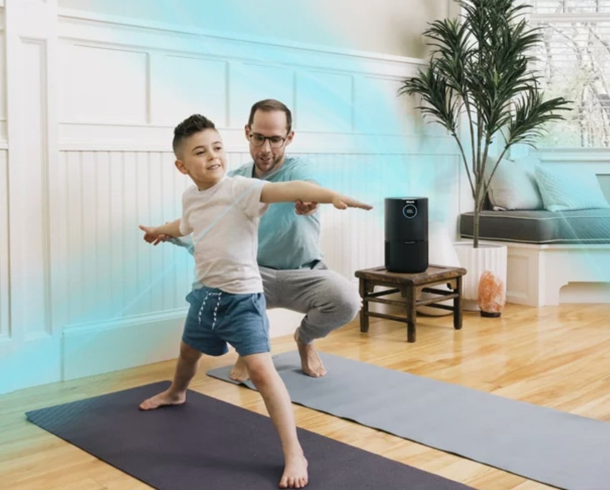 two models doing yoga in the foreground with the black air purifier in the back of the decorated living space
