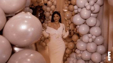kylie jenner doing a little strut into a room surrounded by balloon arches