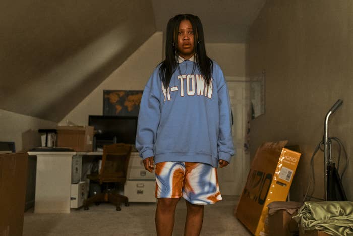 Sad-looking young woman in an oversize sweatshirt and baggy shorts in an attic