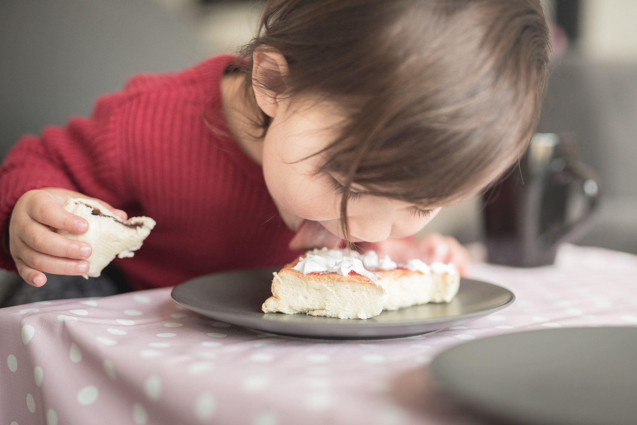 A toddler licking dessert on a plate.