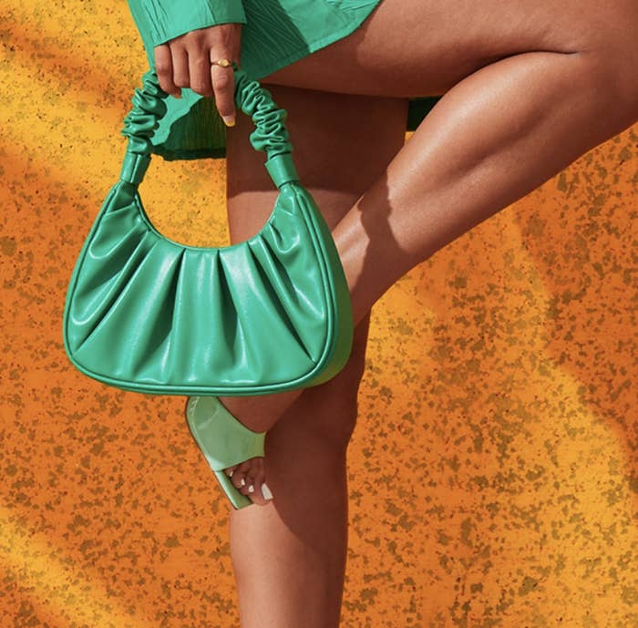 a model holding the bag with their leg bent in front of a bright backdrop