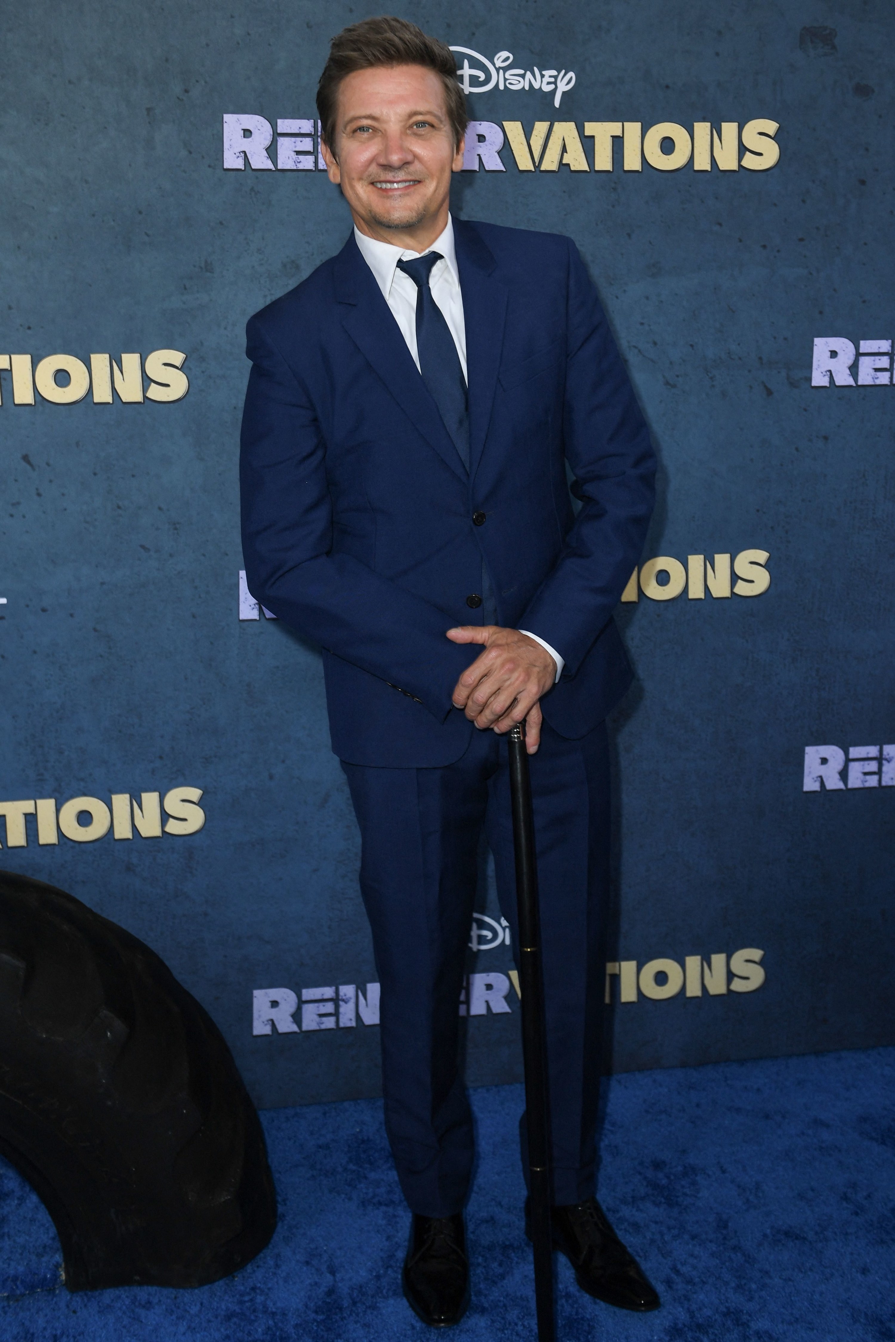 Jeremy smiles on the blue carpet as he holds onto his cane