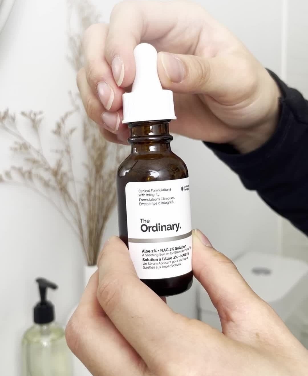 a person opening a bottle of the ordinary serum in a bathroom