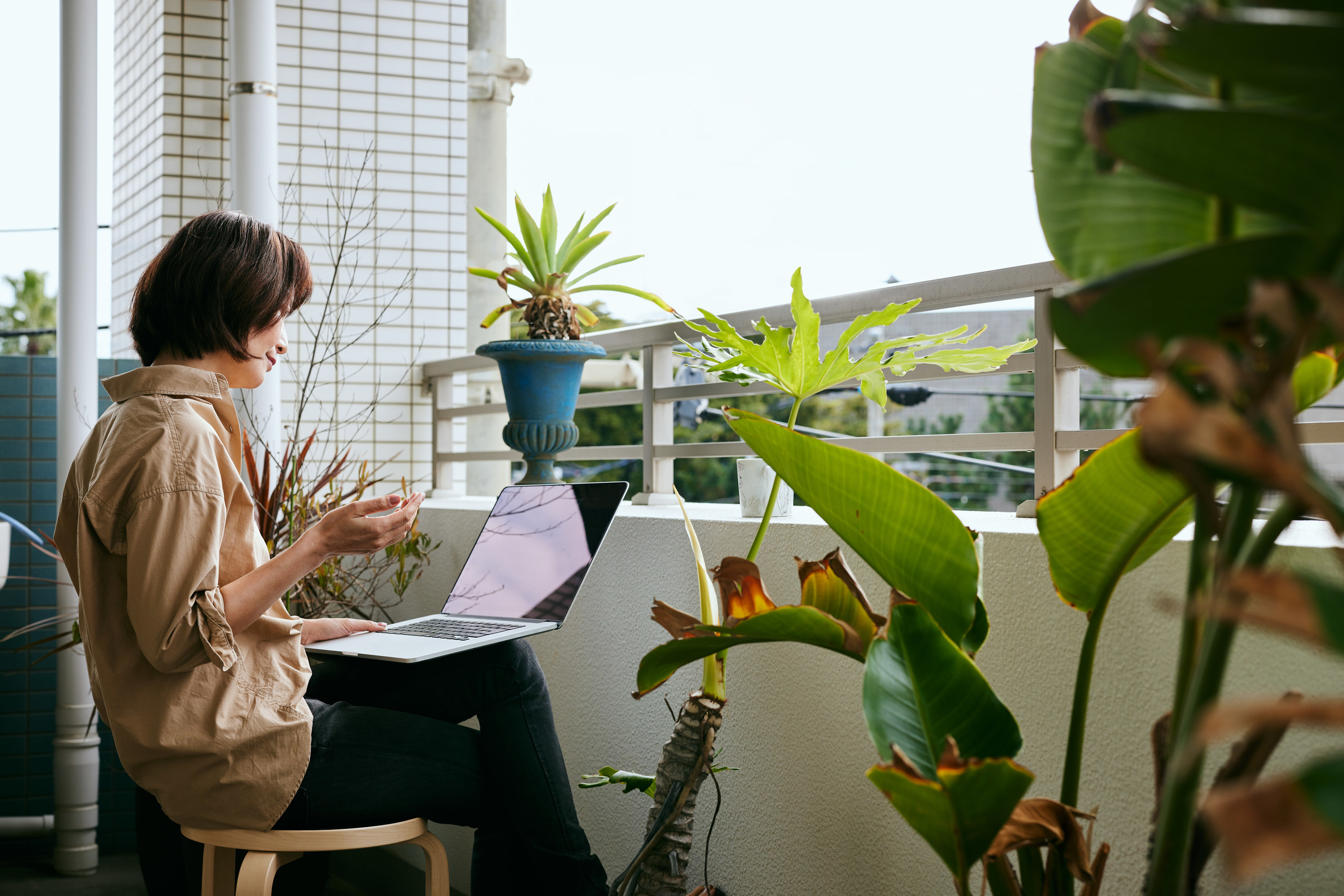 a woman working on a laptop on a patio with plants