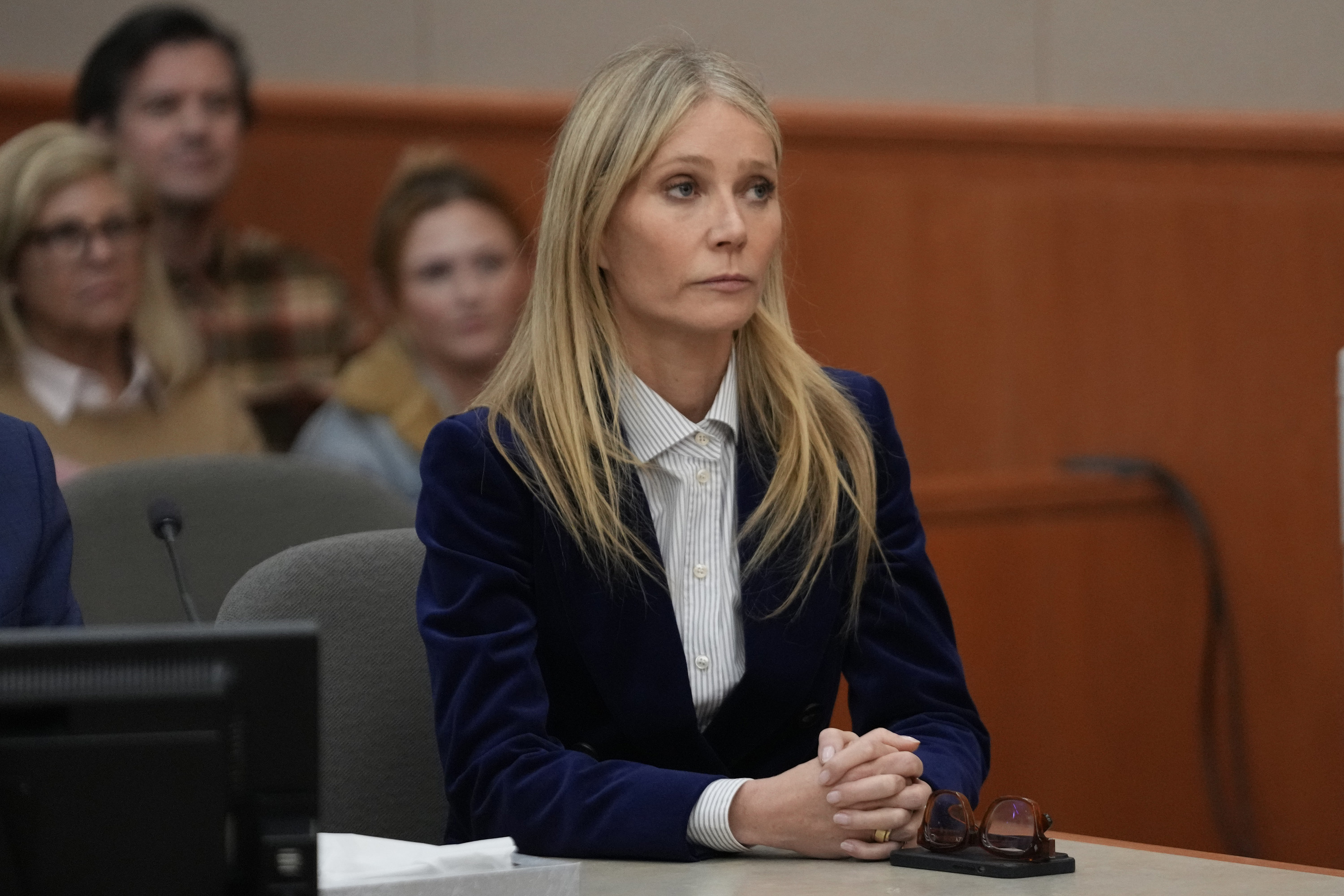 Gwyneth Paltrow, wearing a suit, sitting at the front of a courtroom looking somber