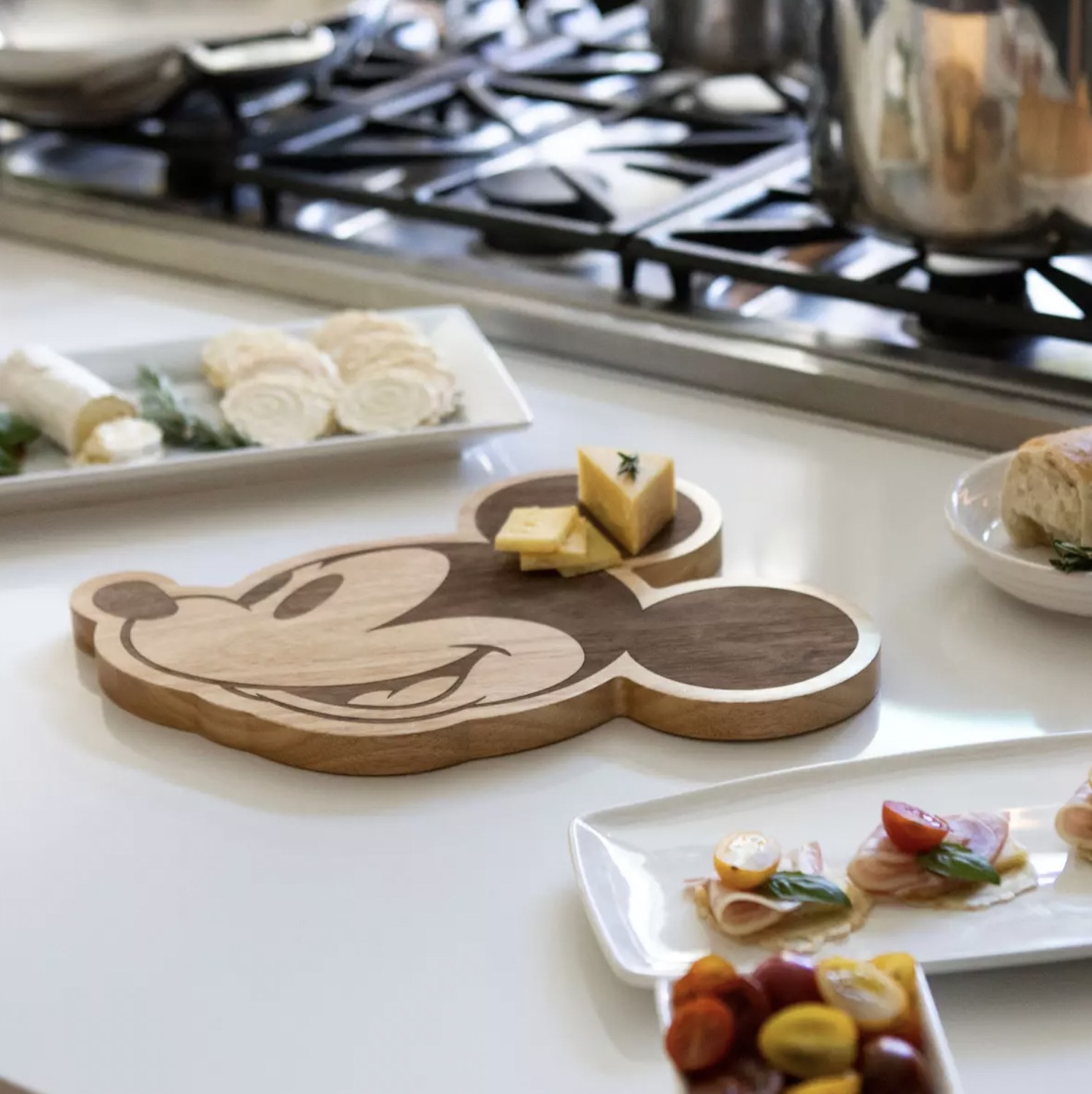 The cutting board with cheese wedge and slices on one ear amongst other platters of snacks on counter