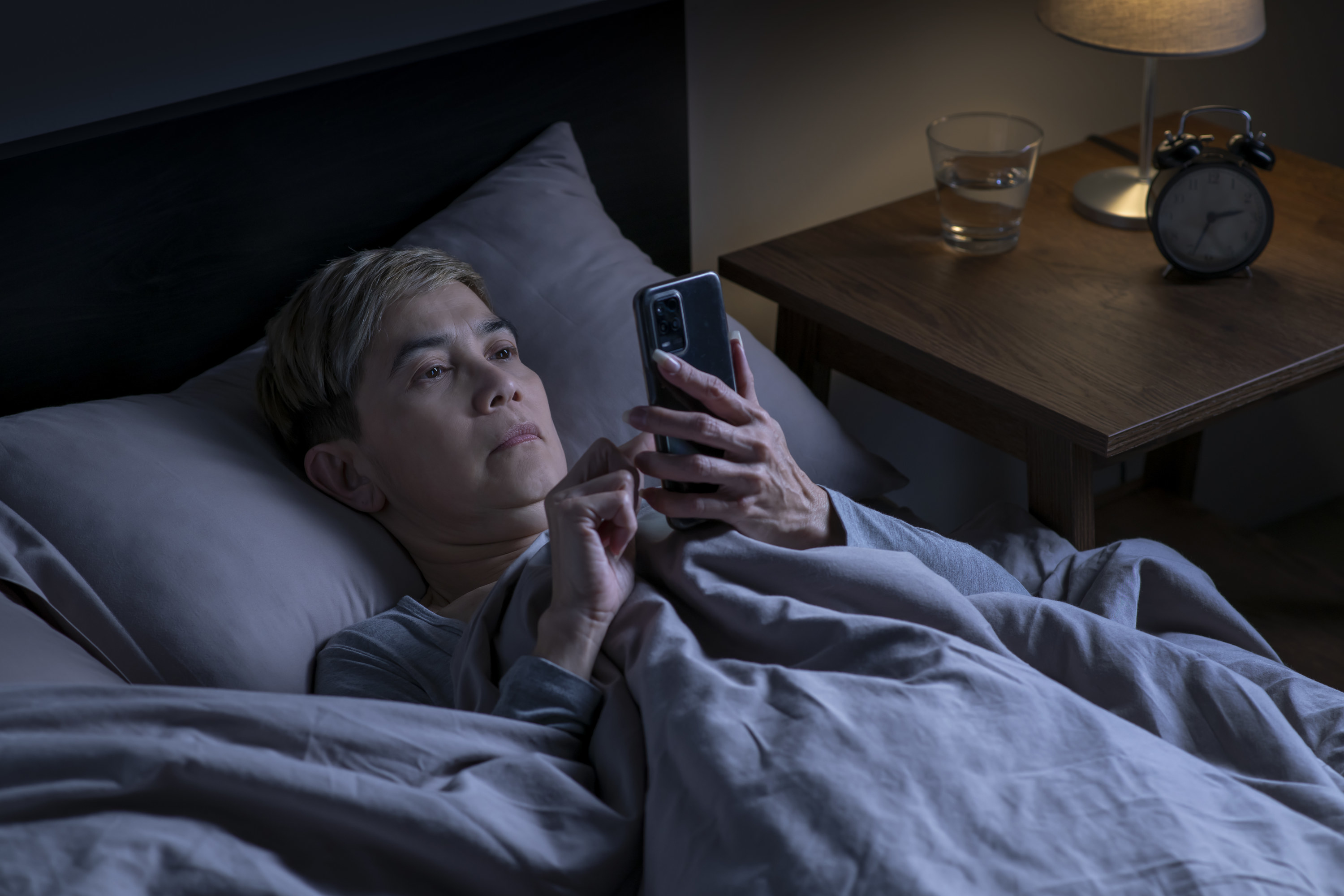 A person scrolling through their phone as they lay in bed