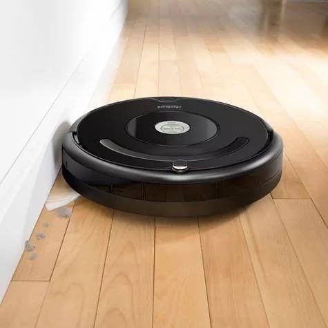 a black Roomba vacuuming dust off a wooden floor