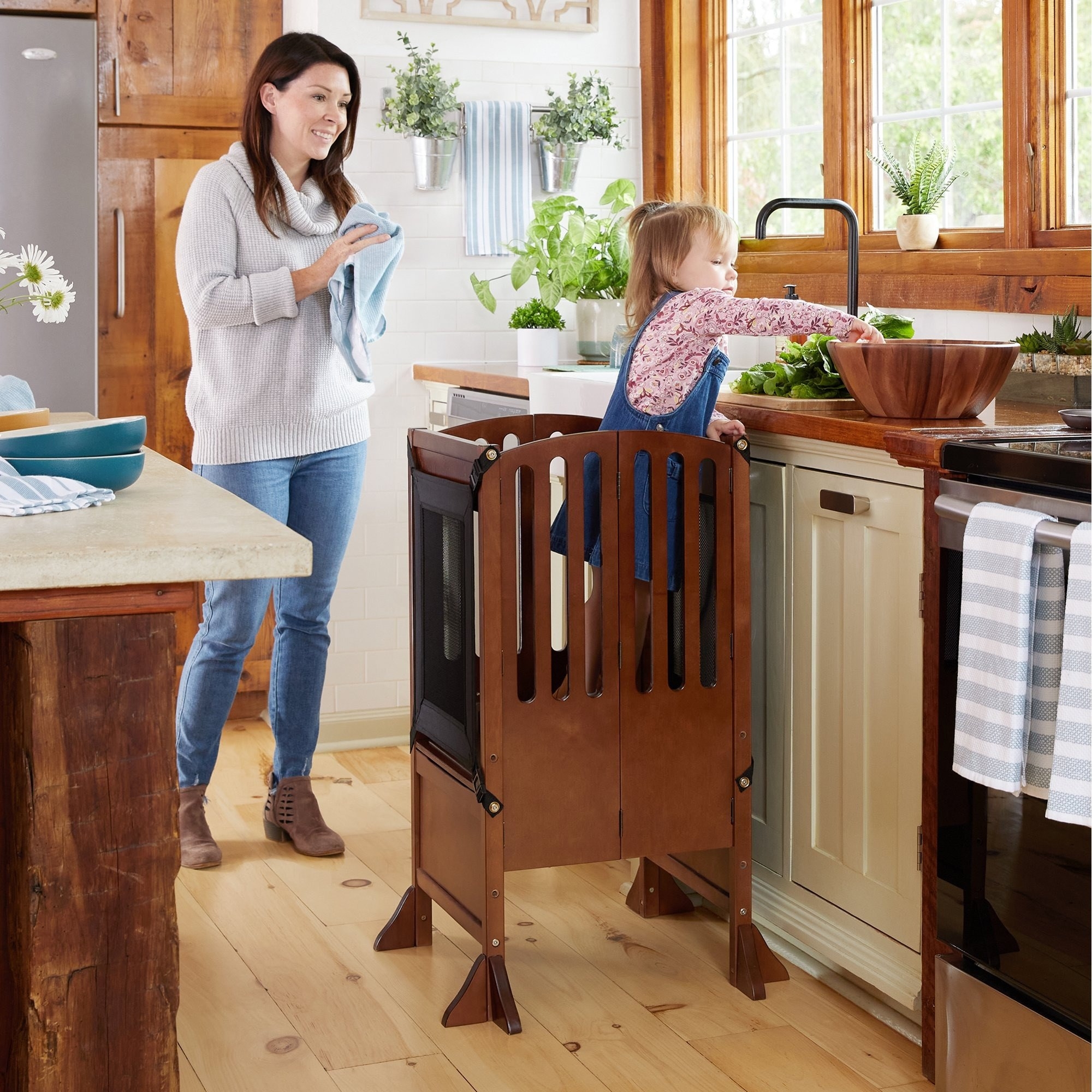 Toddler stands in kitchen helper stool while a parent watches