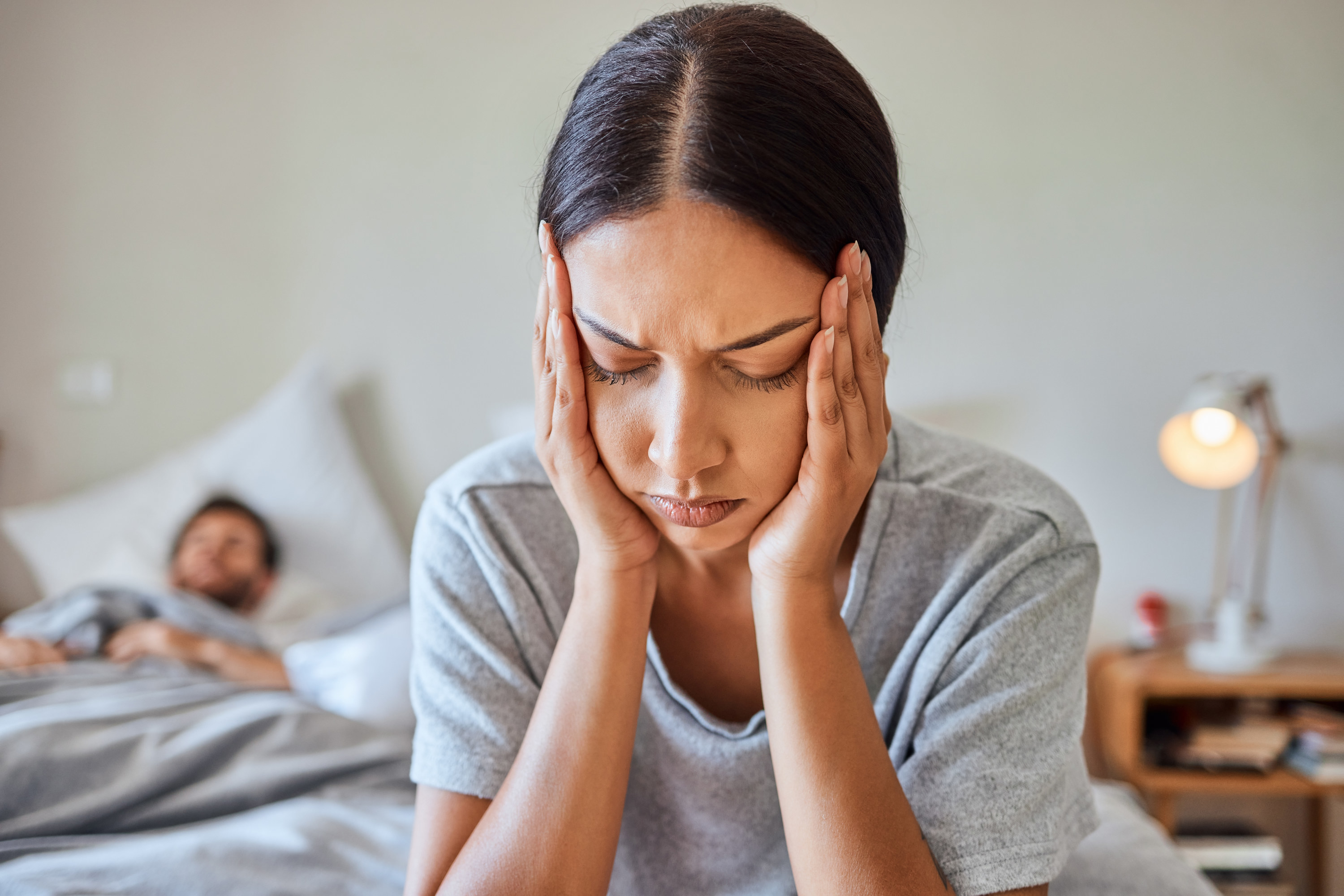 Woman stressing out while partner sleeps in bed behind her