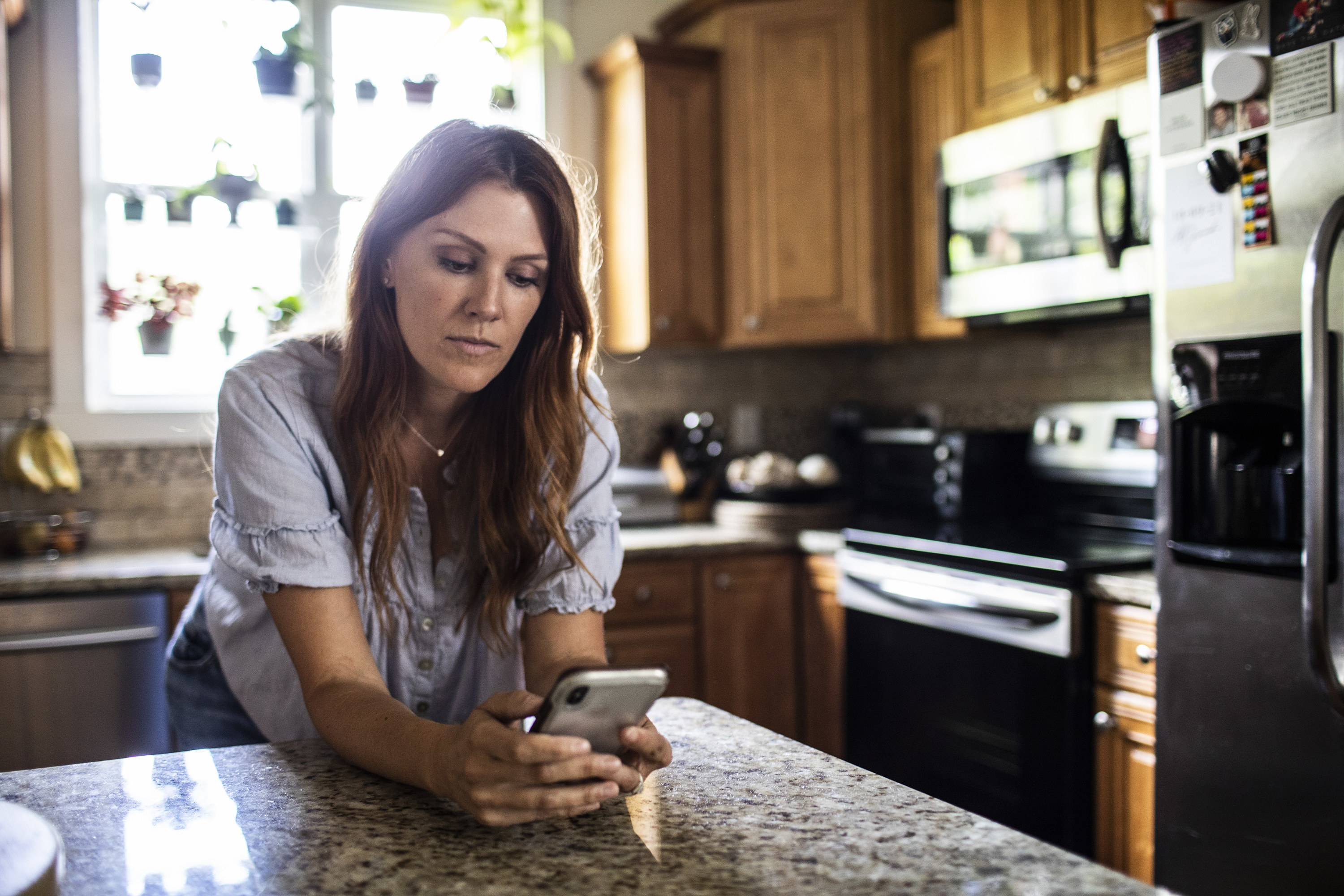 woman looking at her phone while leaning on her kitchen counter