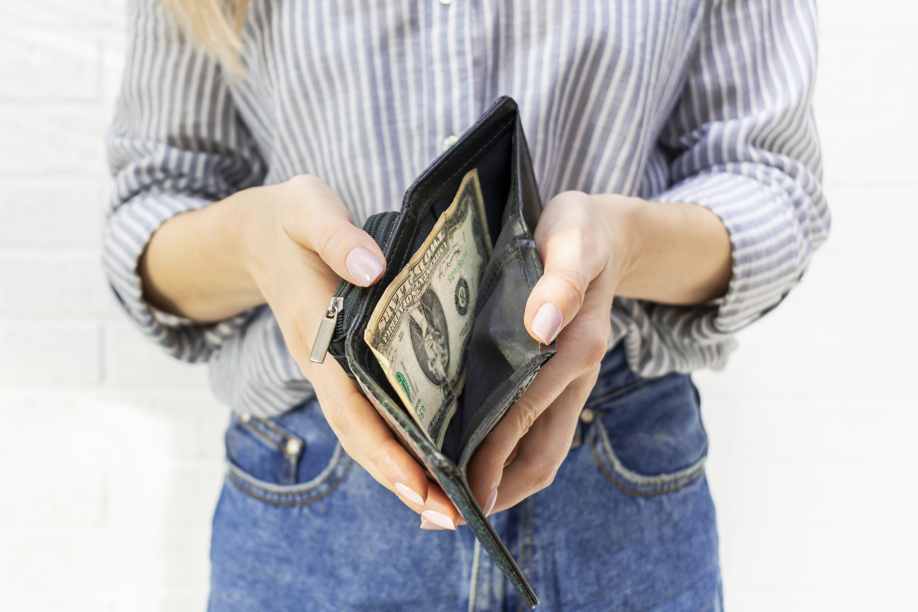 The hands of a young woman hold an open wallet with the last banknote