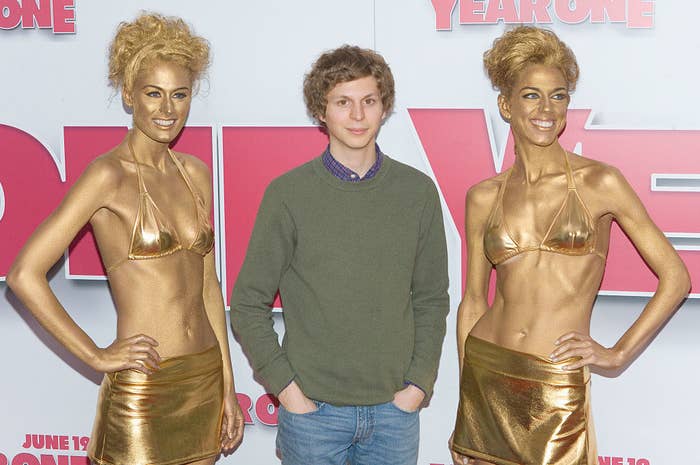 Michael Cera flanked by gold women in bikinis