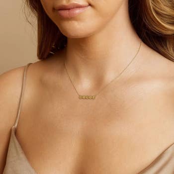 a model wearing a dainty gold necklace with gold bubbles as a nameplate that say 