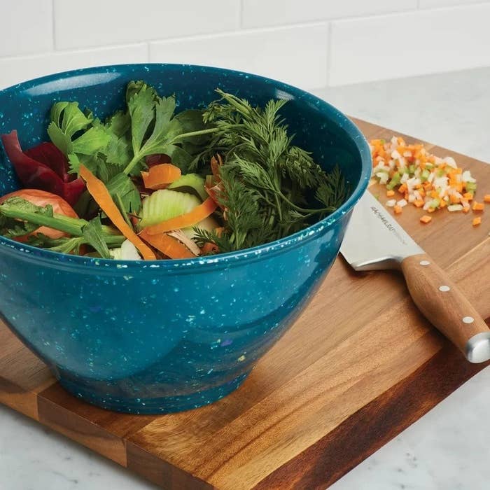 the blue garbage bowl with sliced veggies on a wood cutting board