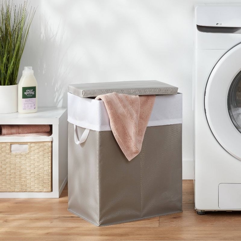 a gray and white laundry hamper with lid in a laundry room with wood floors