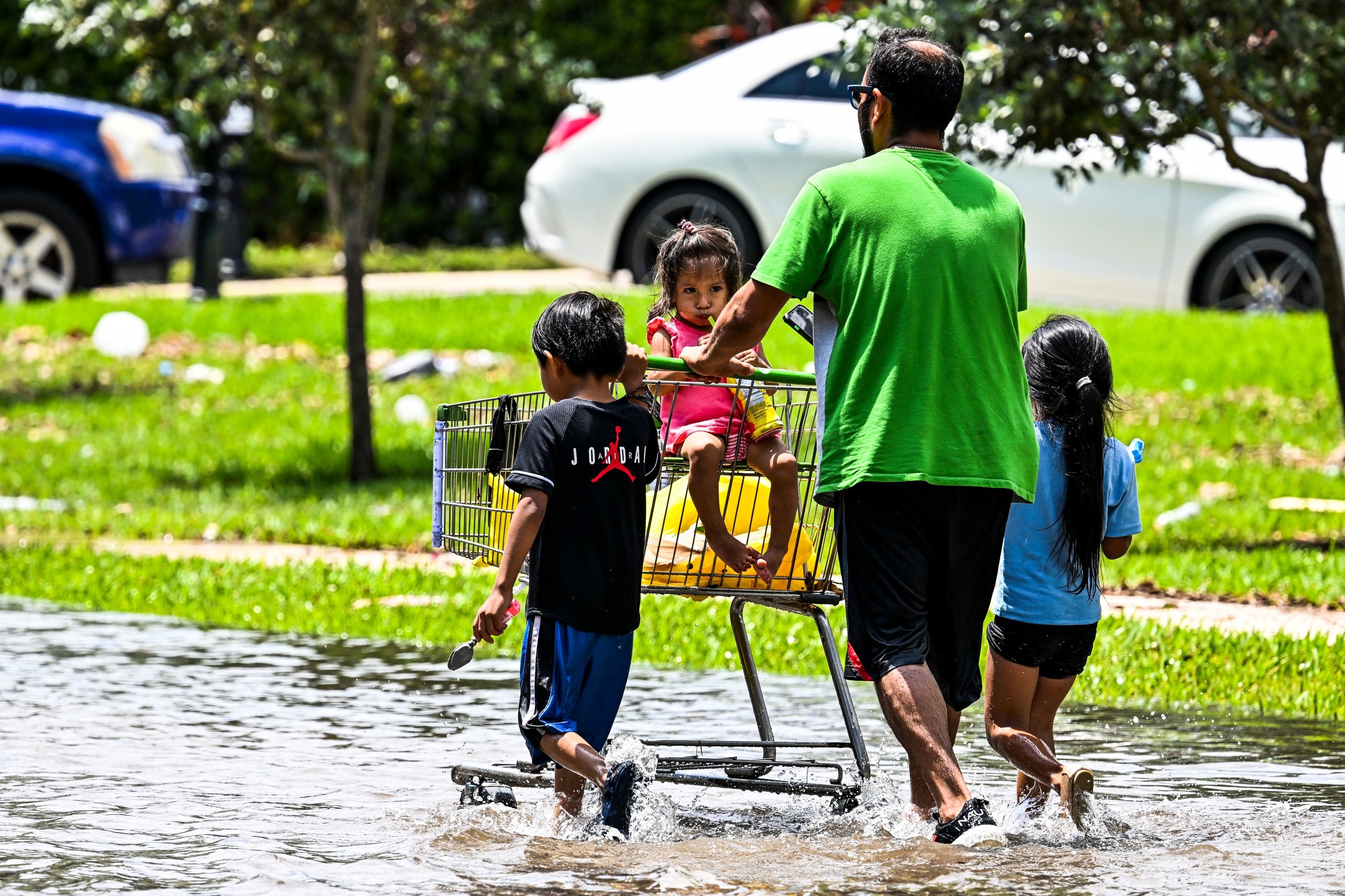 A man walking in water with two children and a third in a shopping cart