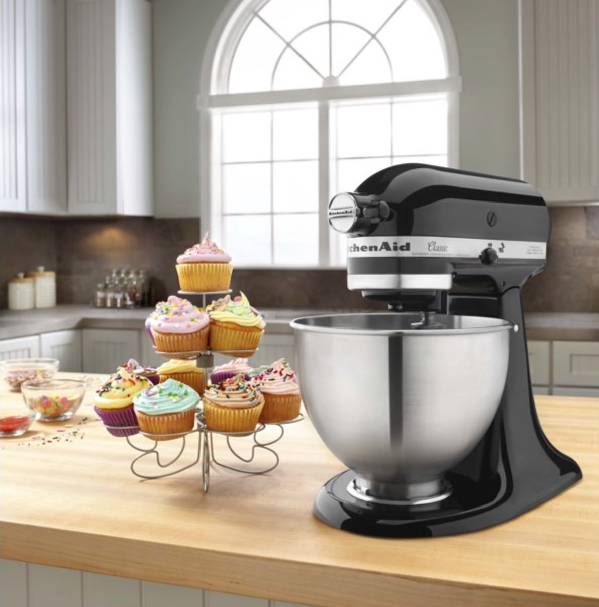 the black stand mixer on a kitchen counter next to a display of cupcakes