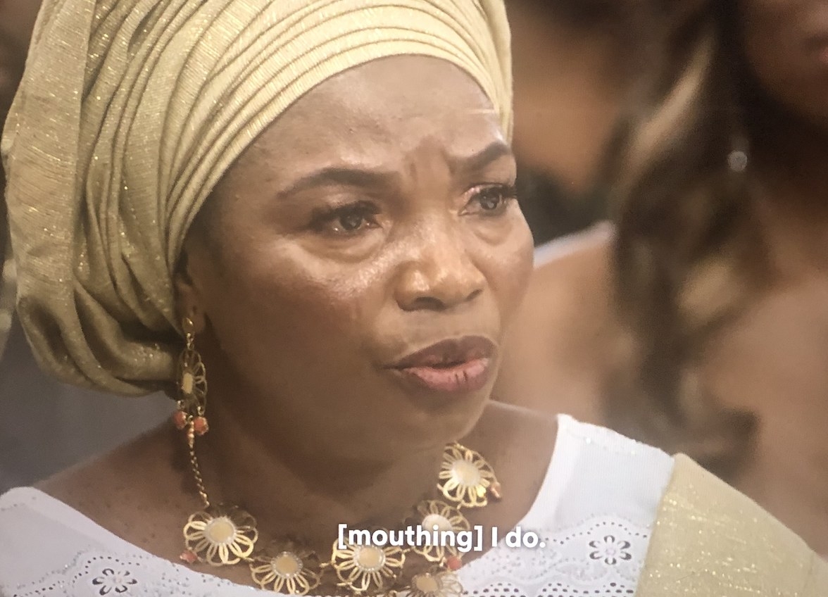 SK&#x27;s mom in a traditional gele with tears in her eyes mouthing the words I do to encourage SK to say yes to Raven