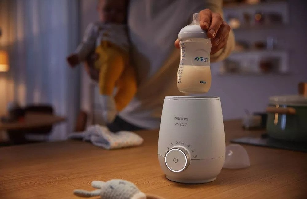 Model&#x27;s hand placing a baby bottle of milk into white bottle warmer device