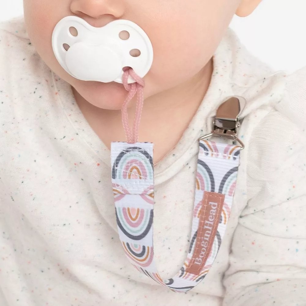 Pacifier clip with rainbow design attached to pacifier in baby&#x27;s mouth and their shirt