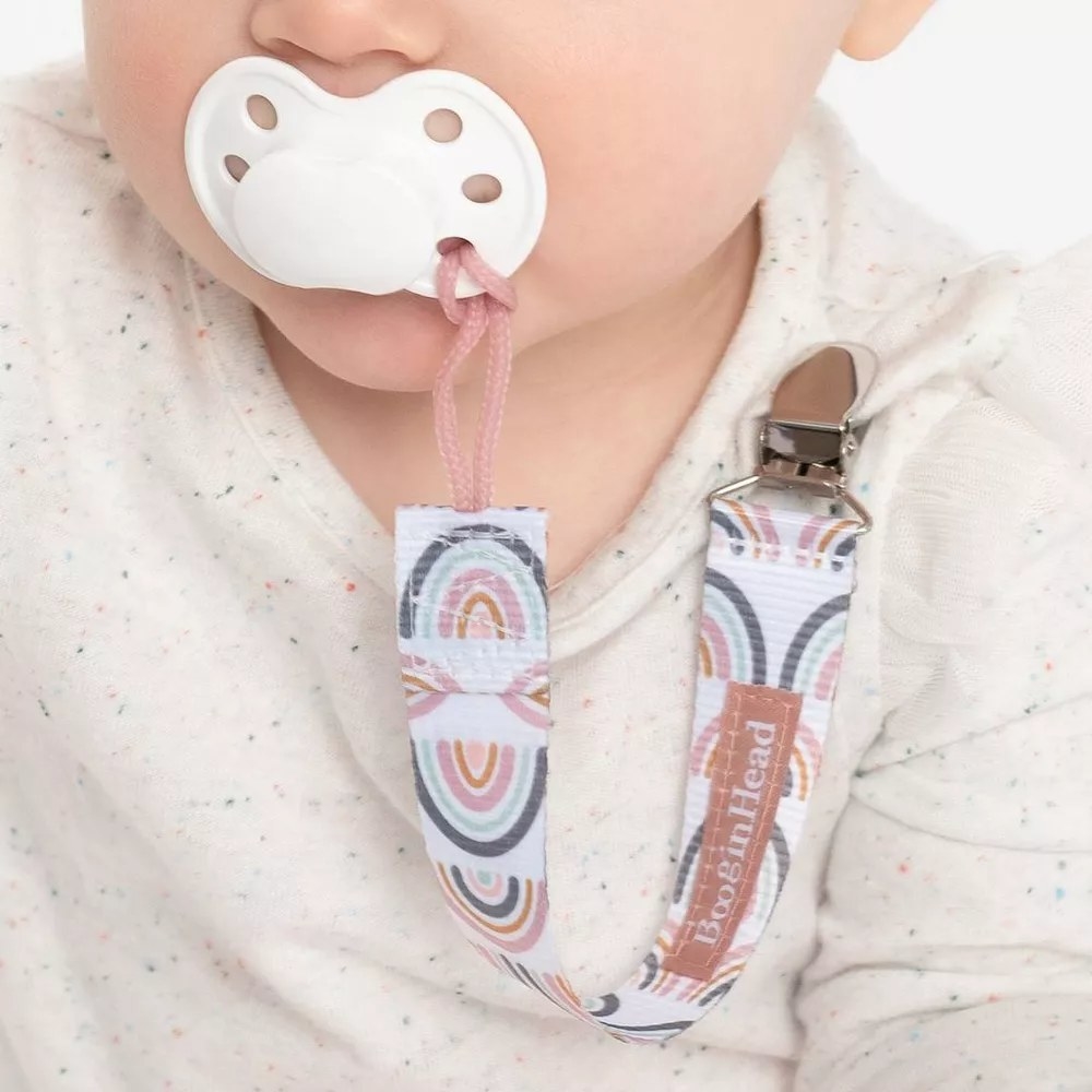 Pacifier clip with rainbow design attached to pacifier in baby's mouth and their shirt
