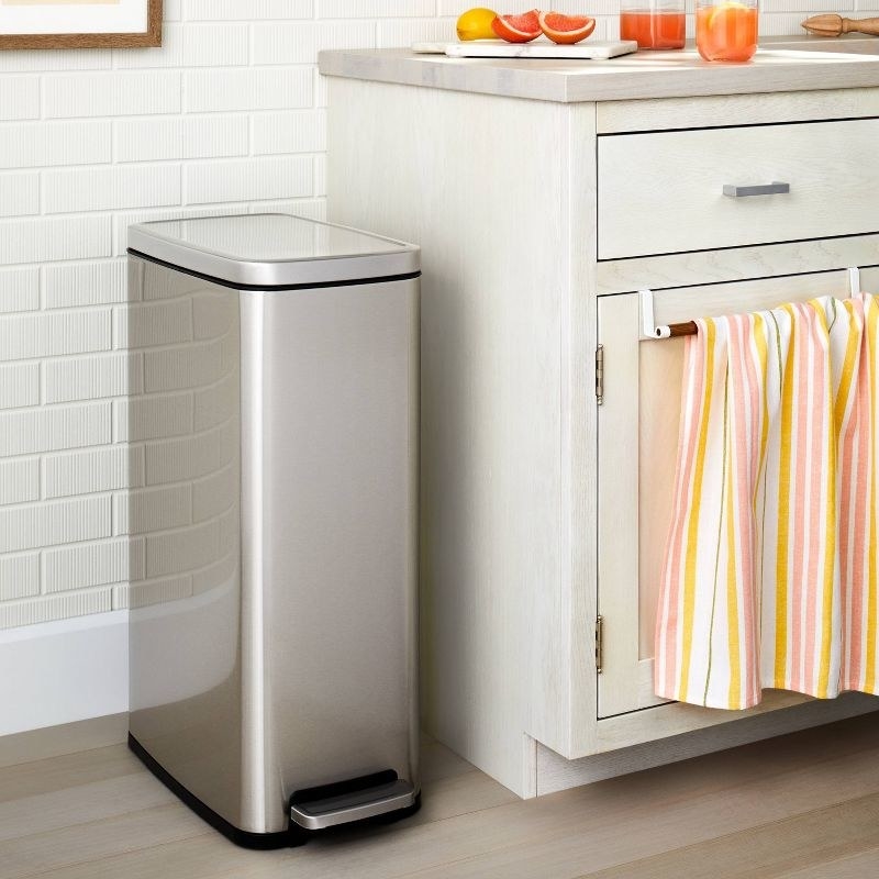 a silver trashcan next to a kitchen countertop with sliced fruit and juices