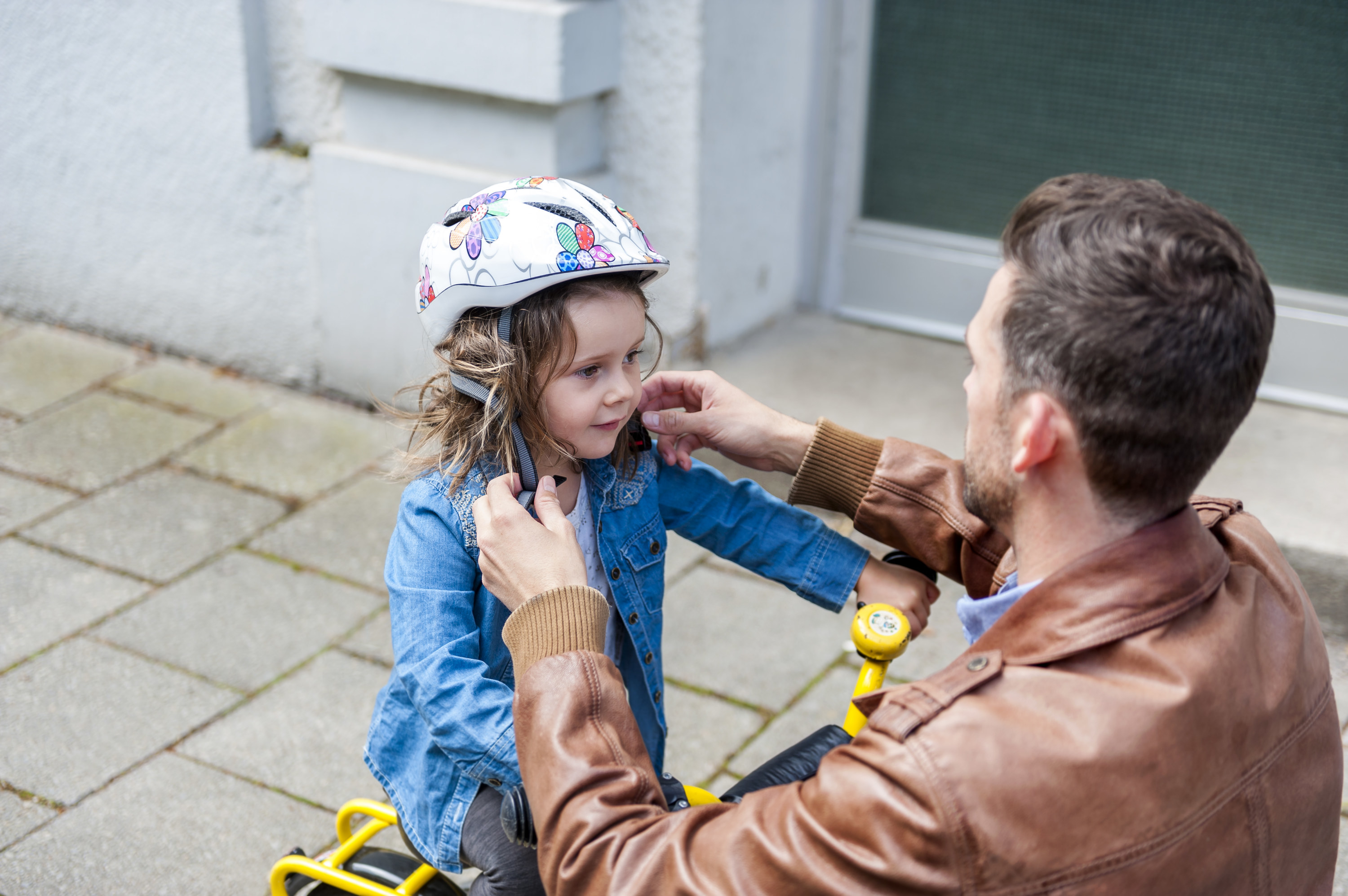 A man fastening his daughter&#x27;s bike helmet