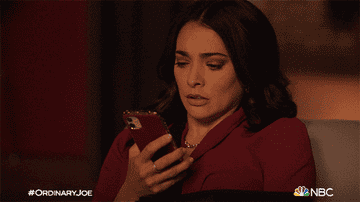 A woman looking at her phone screen before quickly pressing it to her chest and breathing heavily, looking anxious