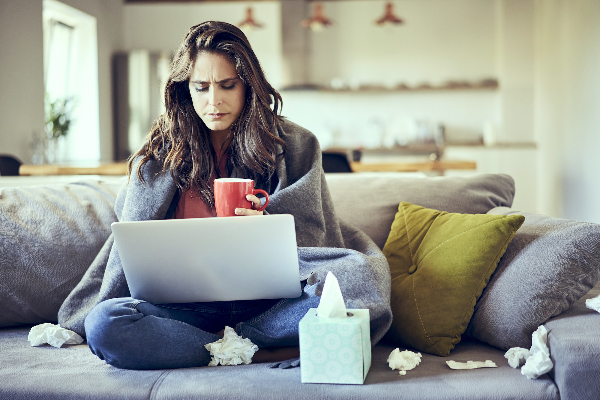 person working from their couch surrounded by kleenex