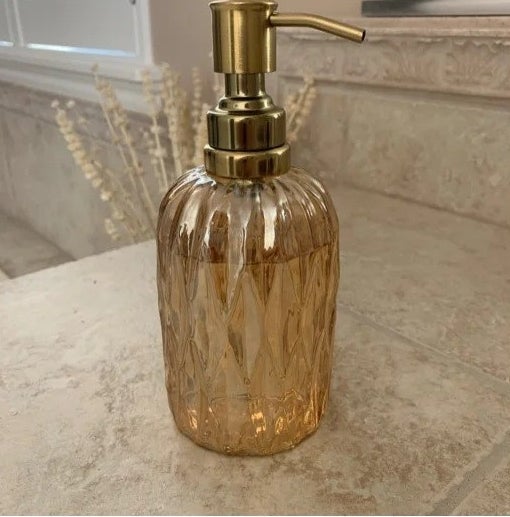 The glass soap dispenser with a gold top on a bathroom counter