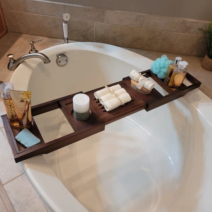A reviewer photo of the bath caddy holding multiple items over a bathtub