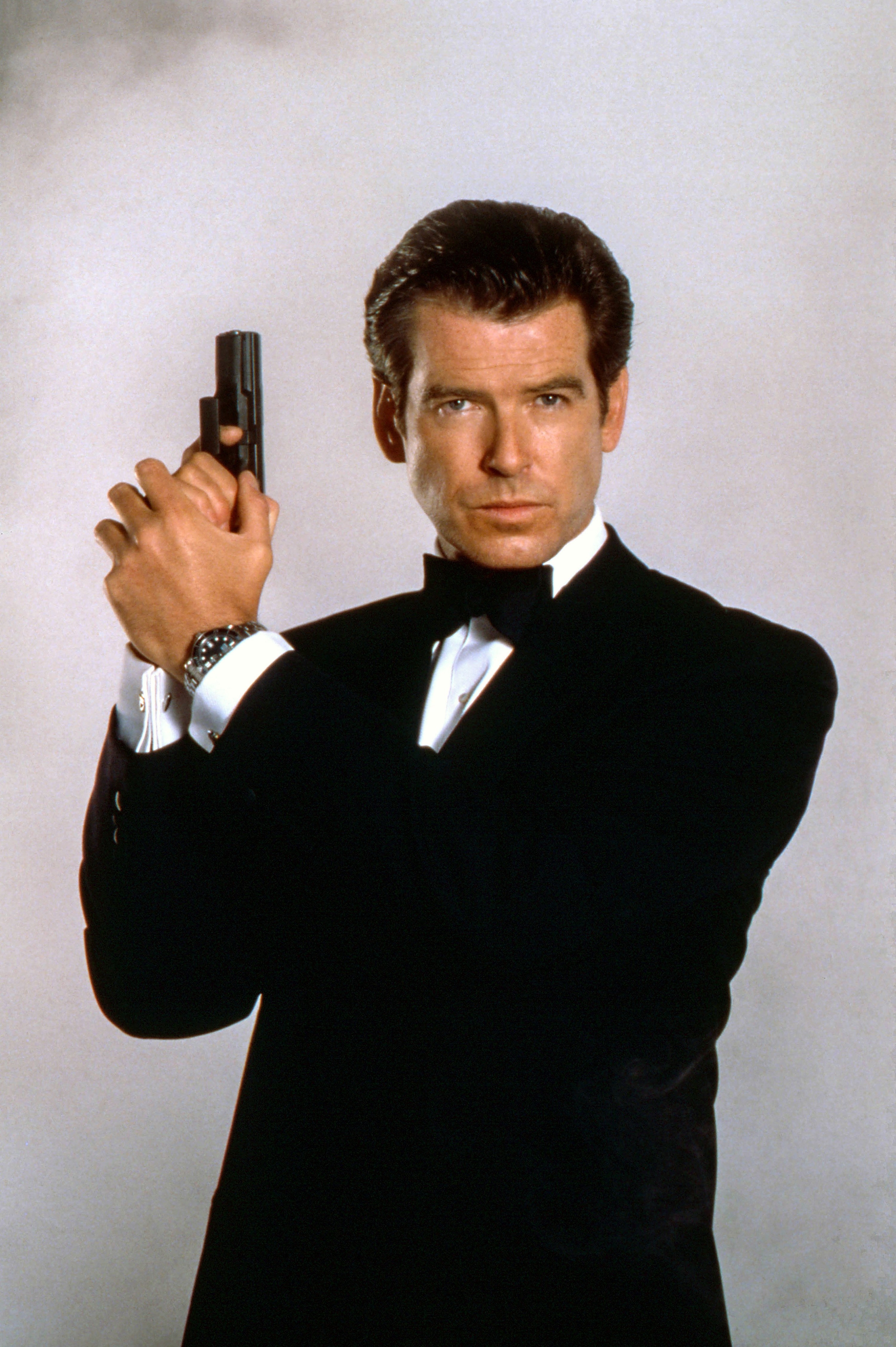 Pierce in a tux and holding a gun