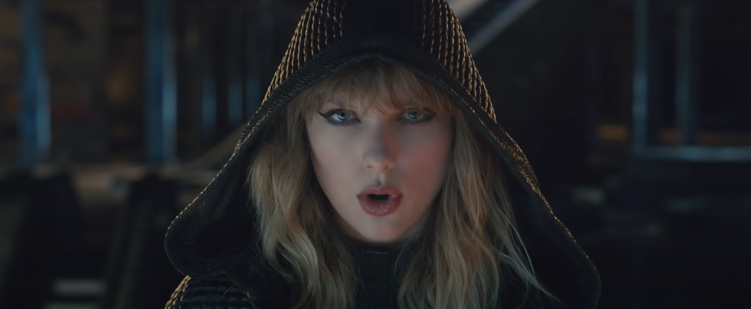 Taylor Swift with a black hood on looking at the camera.