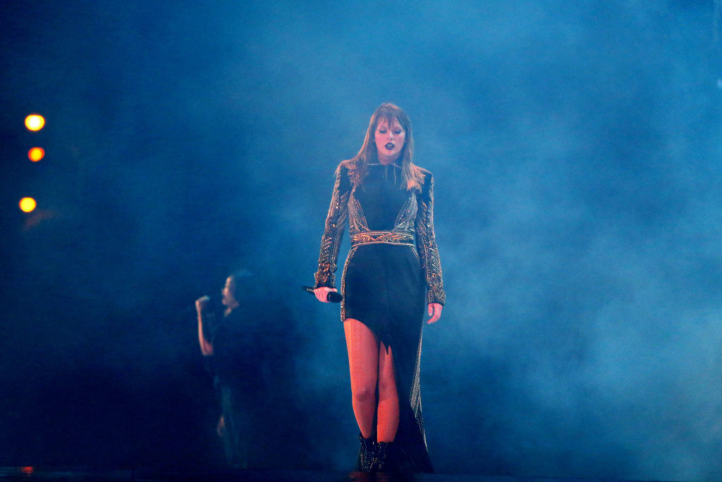 Taylor Swift in a black dress walking through fog on stage.
