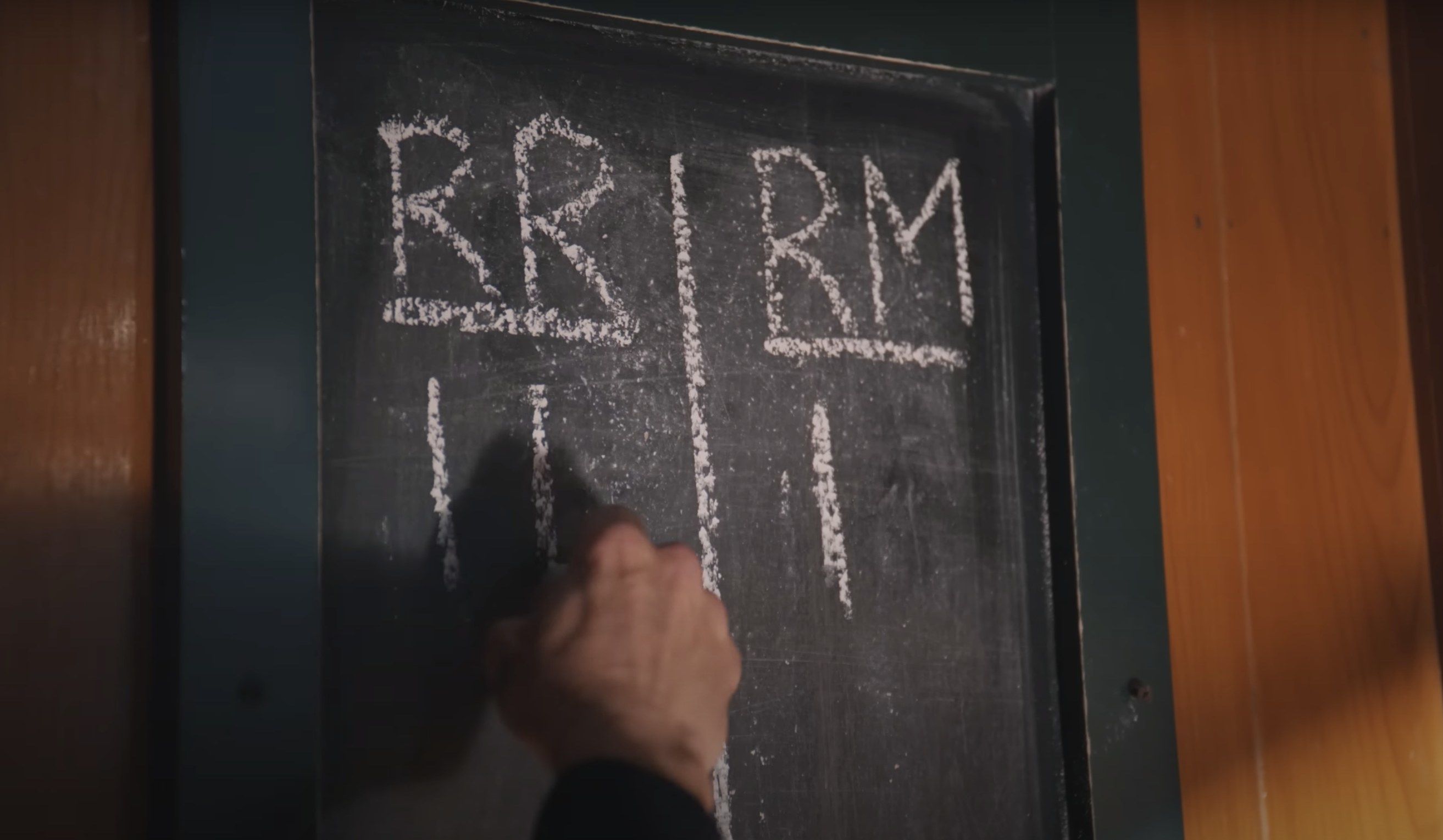 A chalkboard that says RR and RM and hand adds a roman numeral 2 under RR
