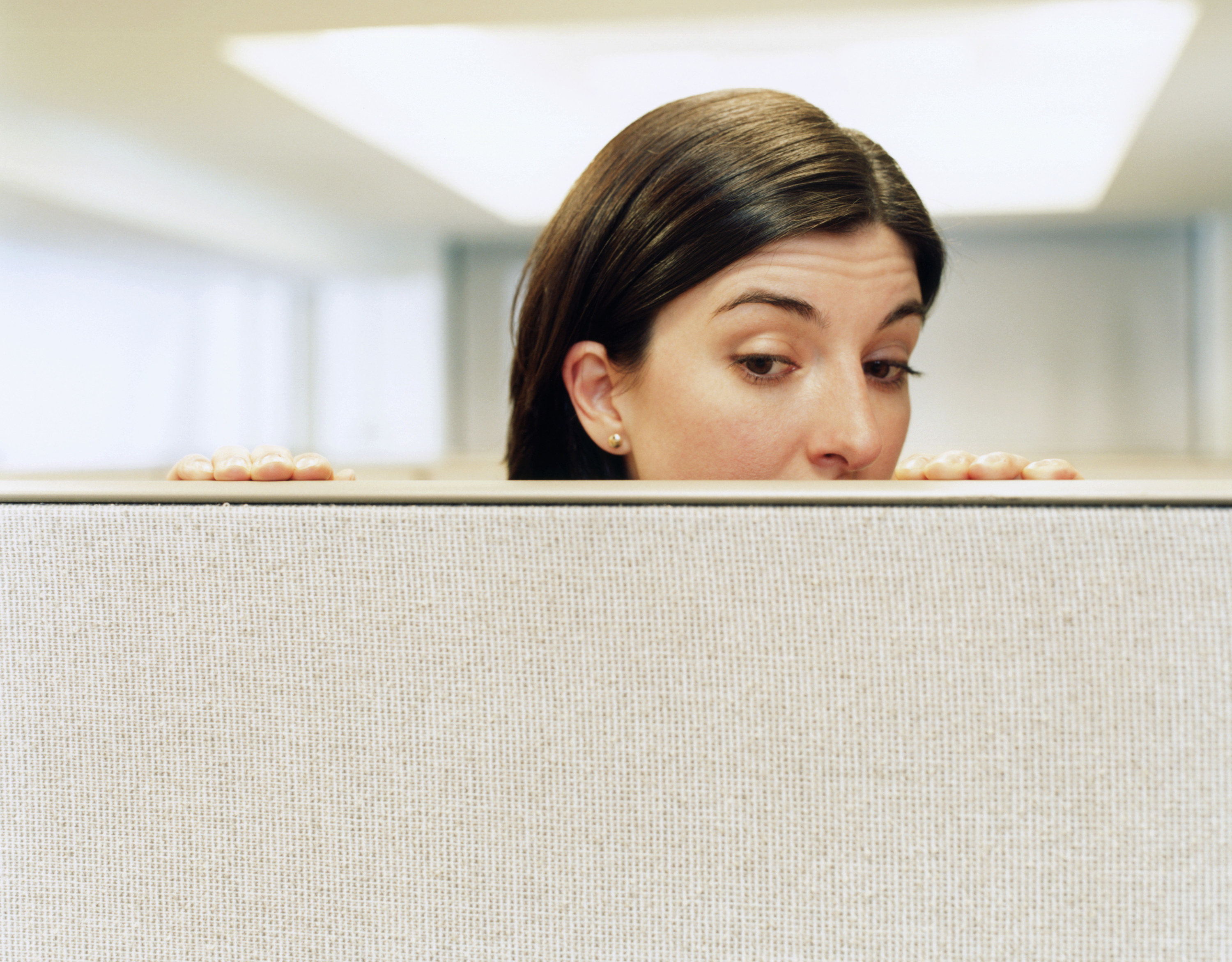 A woman peeking over a cubicle wall