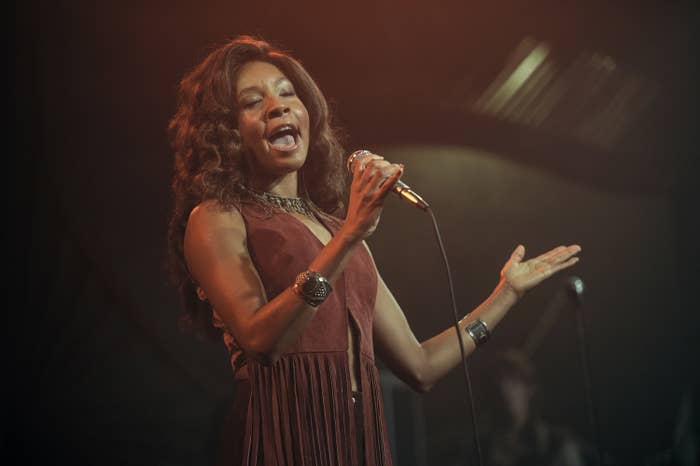 The actress is wearing a maroon dress and singing into a microphone.